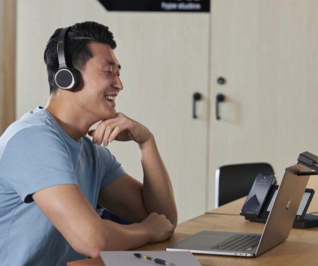 Homem sentado em uma mesa de escritório, sorrindo, usando fones de ouvido 