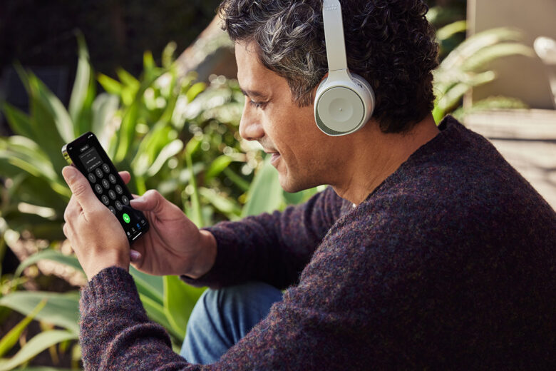 Pessoa sentada em ambiente externo usando um fone de ouvido de trabalho e Webex Go em seu dispositivo móvel.
