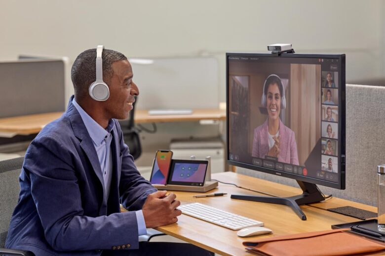 A smiling professional in a blue blazer and a headset collaborates with several colleagues on a virtual meeting via Webex