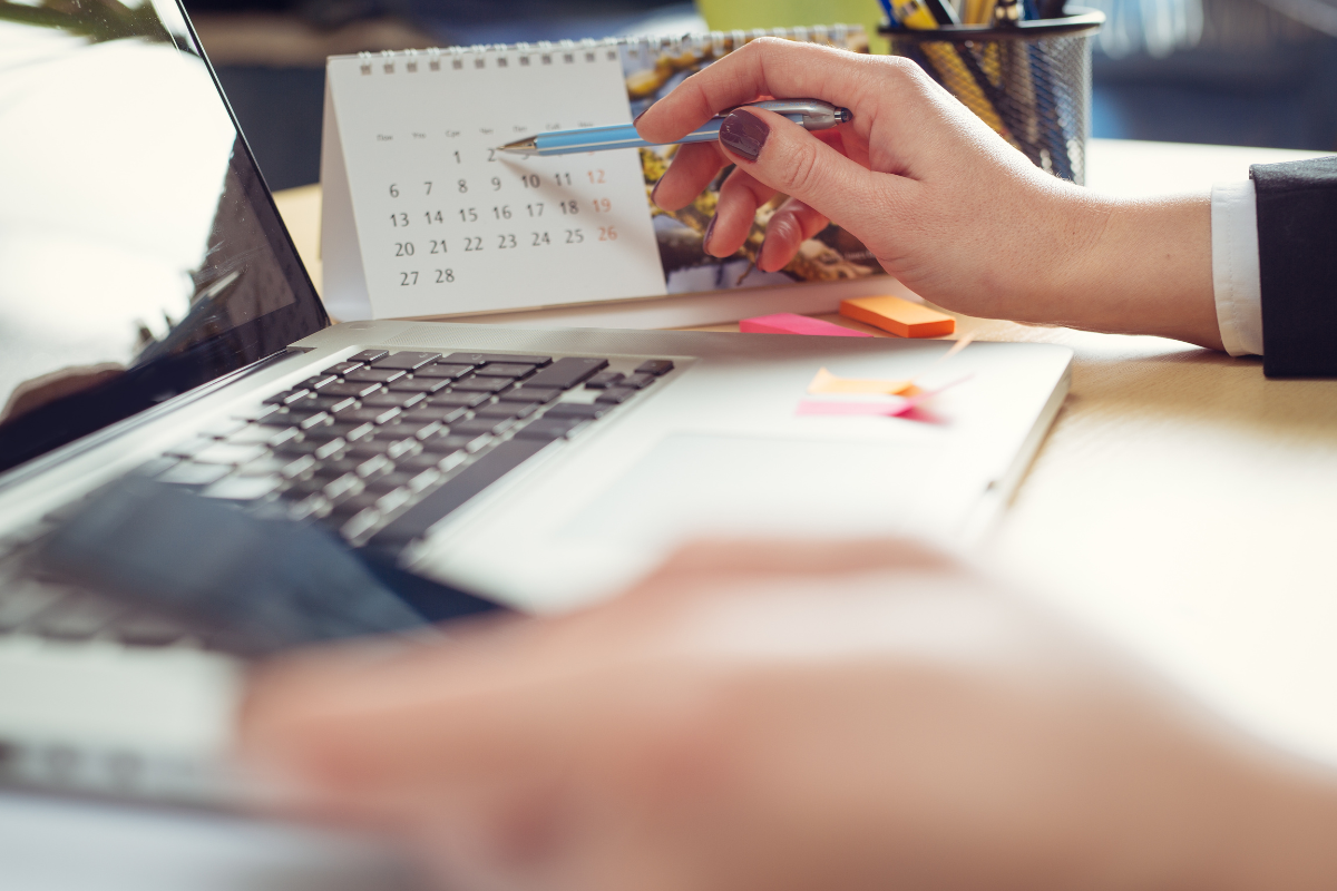 Person holding a pen to a calendar and a phone in other hand