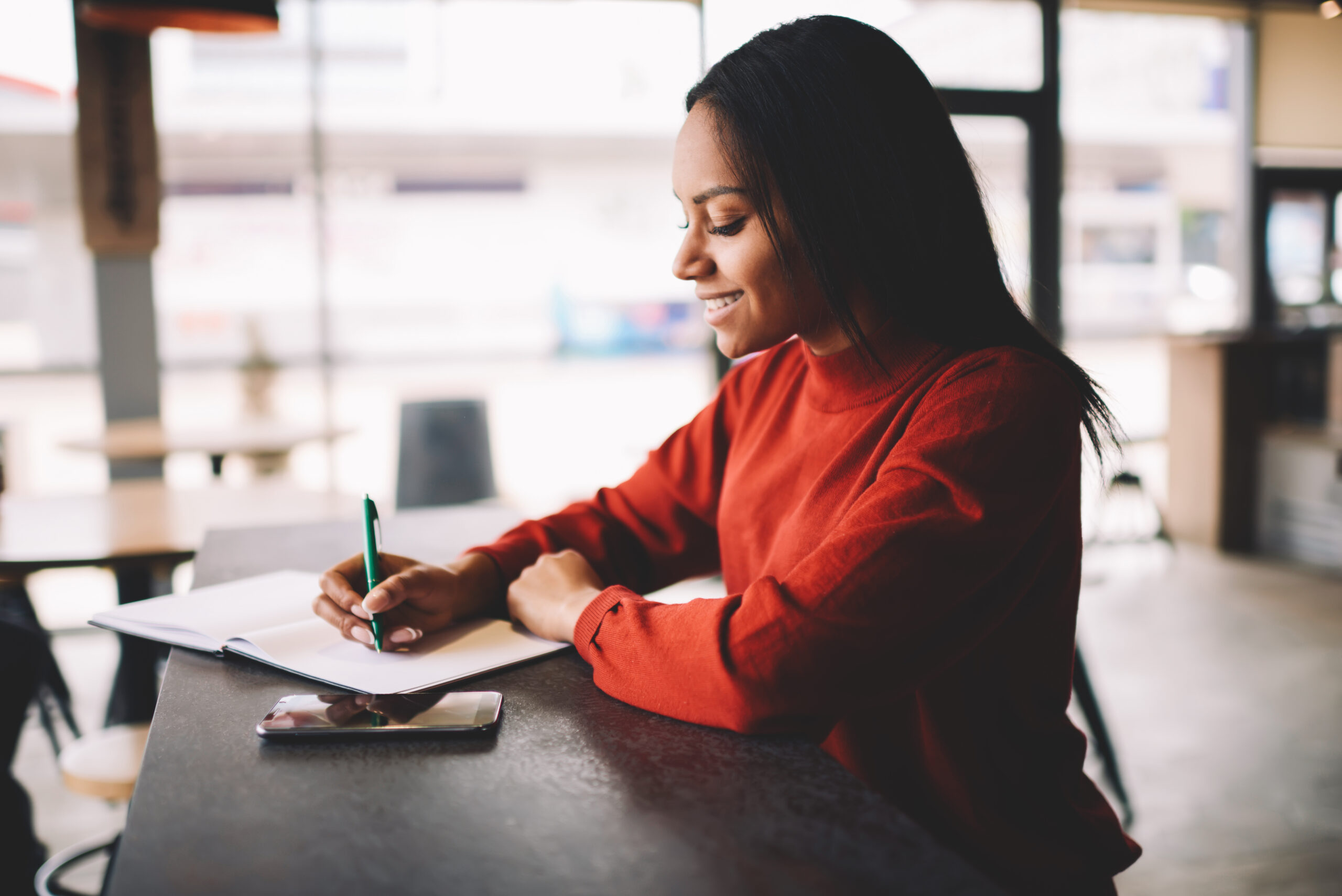 Cheerful African-American woman sits at desk with checklist