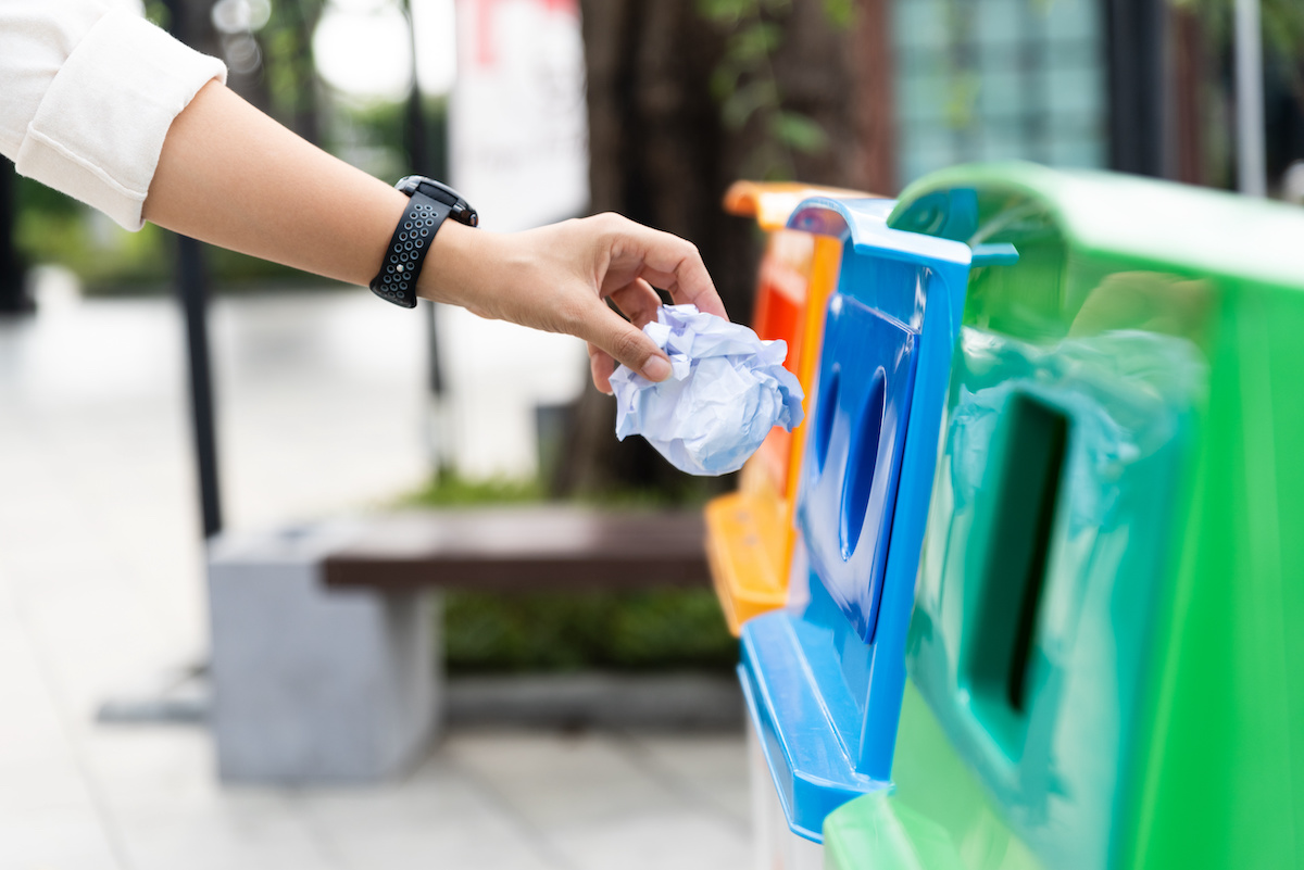 Closeup portrait woman hand throwing crumpled paper in recycling bin.