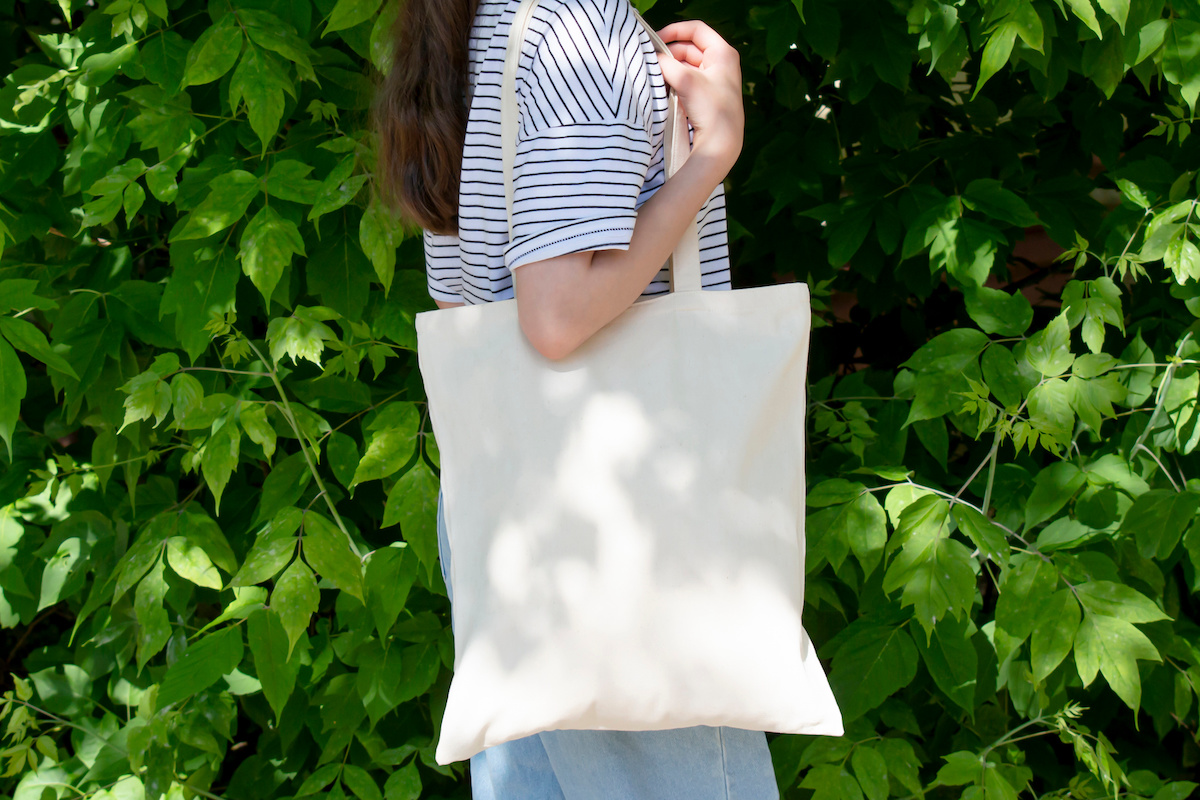 Empty reusable canvas tote bag mockup. Natural canvas eco-friendly shopper bag on girl's shoulder. Mockup for presentation of design or brand