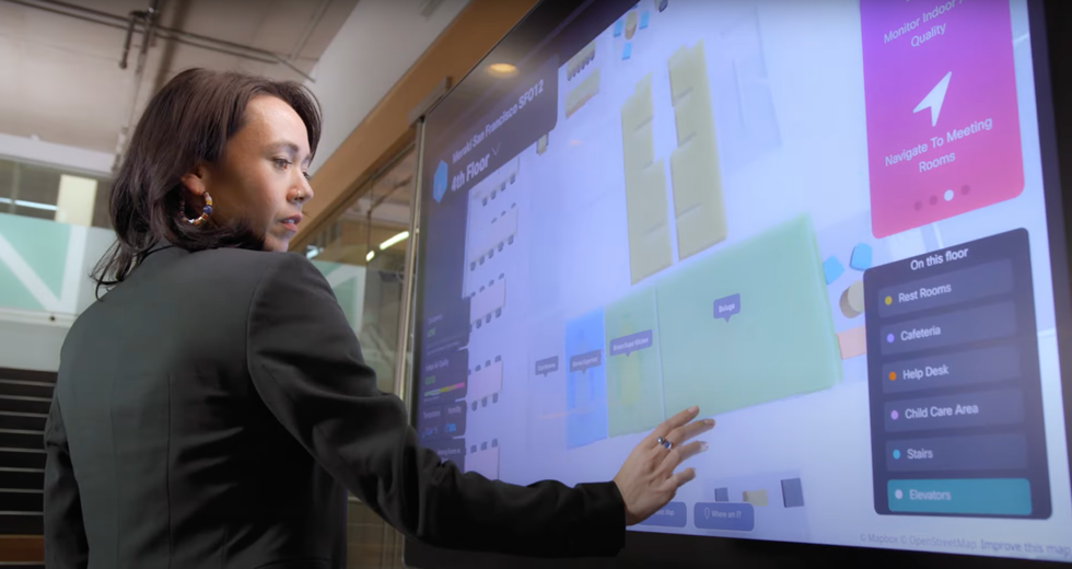 Female Employee Using Touch Screen, Connected By Cisco Spaces, To Navigate The Floor Plan To Her Office