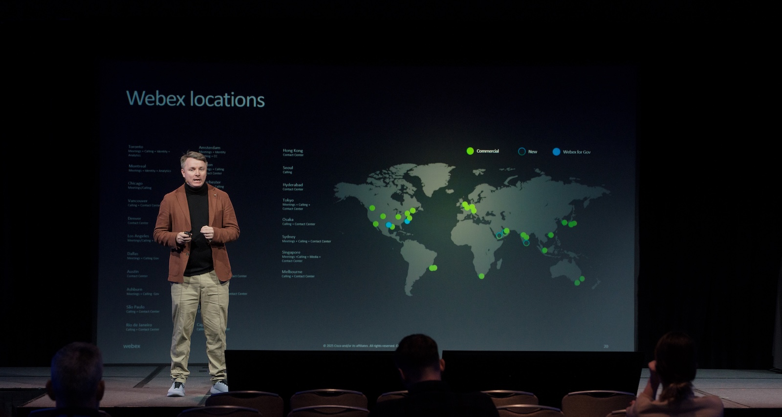 A presenter speaks at WebexOne while a large presentation screen shows a global map highlighting Webex locations, including commercial, government, and new regional deployments.