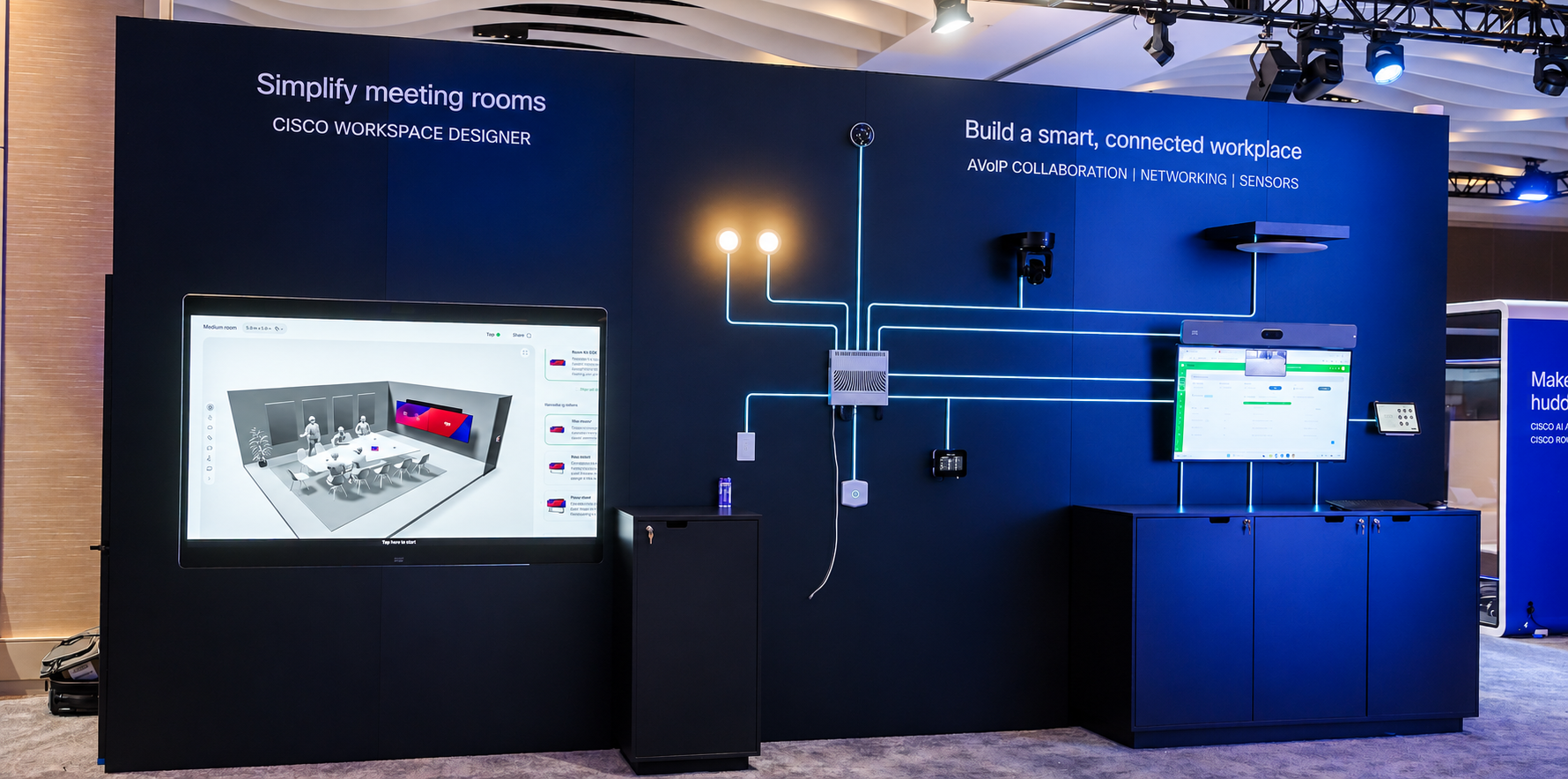 Alt text: Cisco Workspace Designer exhibit showing a meeting-room layout alongside connected workplace devices, including displays, cameras, sensors, and controls.